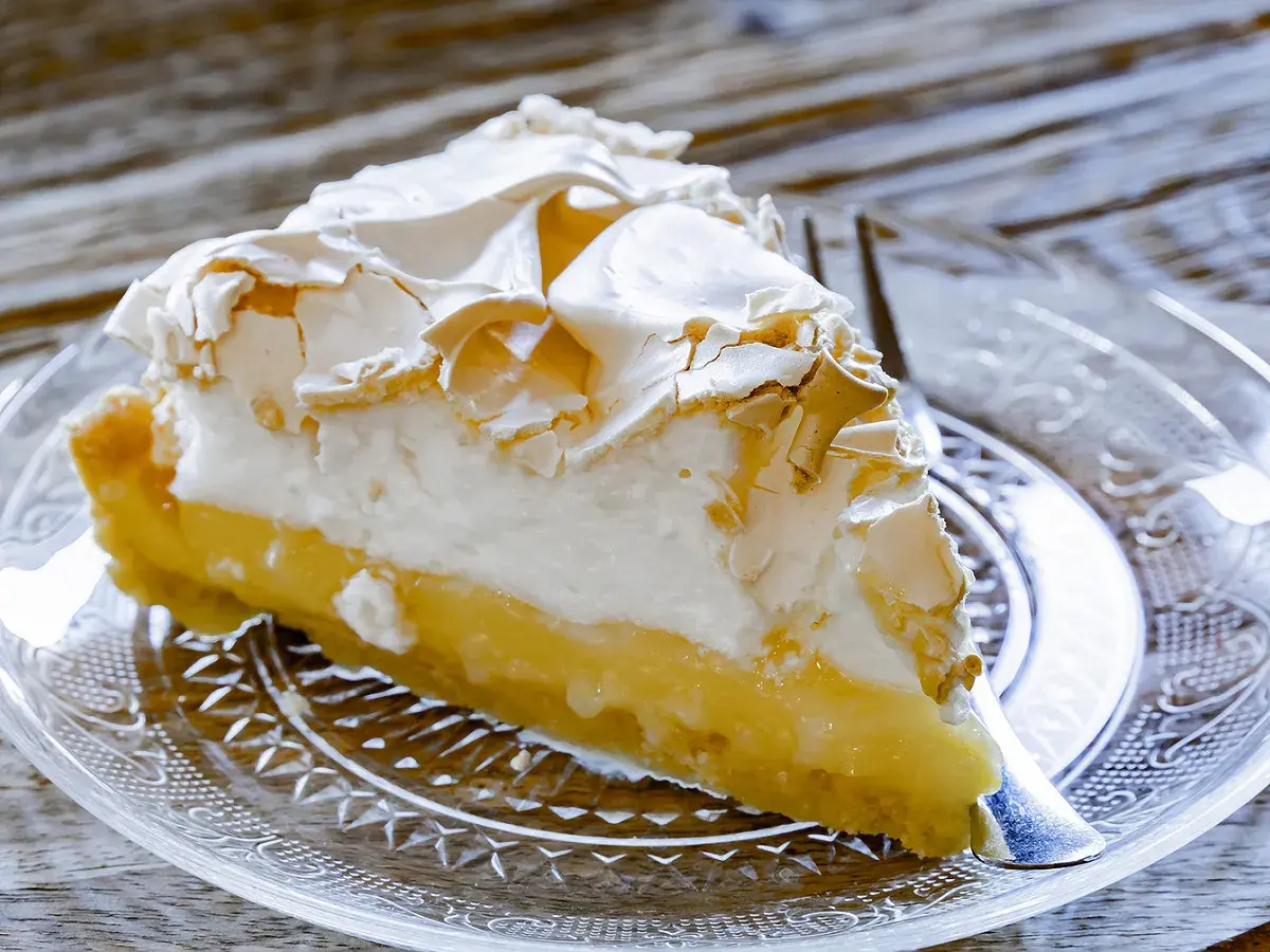 Une part de tarte au citron meringuée, avec sa crème jaune acidulée et sa meringue dorée, prête à être dégustée.