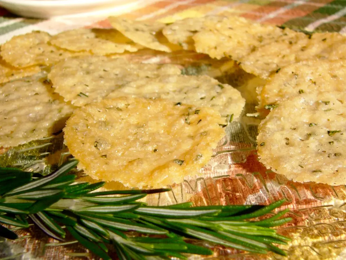 Délicieuses tuiles parmesan poêle, croustillantes et dorées, parsemées d'herbes. Une branche de romarin frais ajoute une touche aromatique.