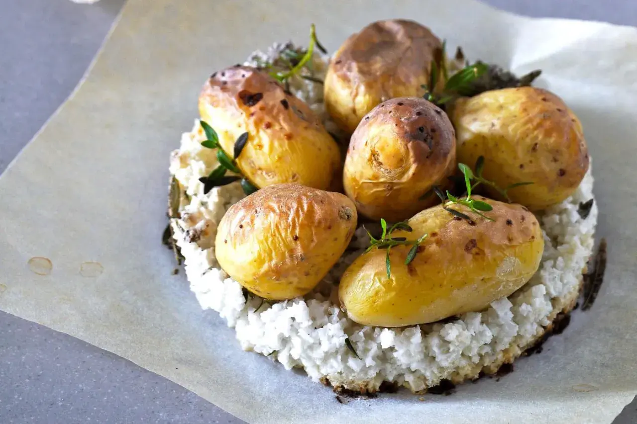 Pommes de terre nouvelles dorées, garnies d'herbes fraîches, sur un lit de purée de chou-fleur. La cuisson pomme de terre nouvelle est réussie.
