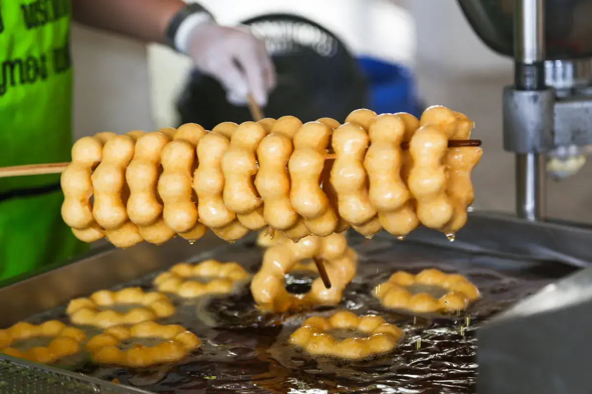 Des beignets dorés, en forme de chaînette, sont frits dans l'huile. La pâte à beignets prend forme, prête à être dégustée.
