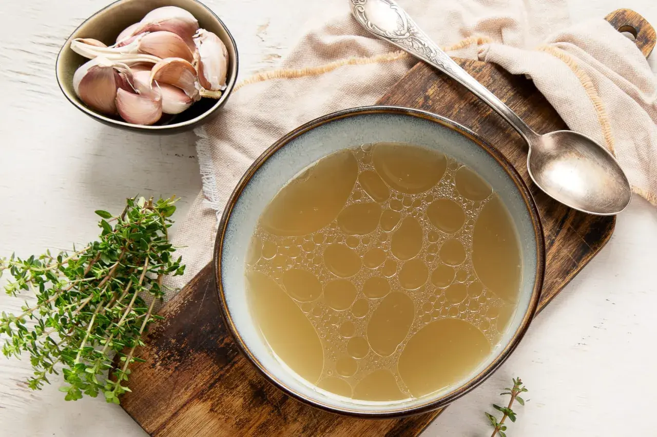 Un bol de bouillon de volaille doré, avec de l'ail et du thym. Idéal pour savoir comment faire un bouillon de volaille savoureux.