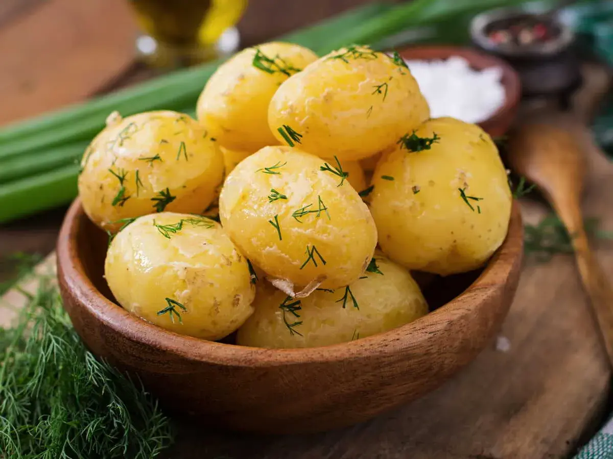 Pommes de terre à l'eau, tendres et parsemées d'aneth frais, dans un bol en bois. Un plat simple et savoureux.