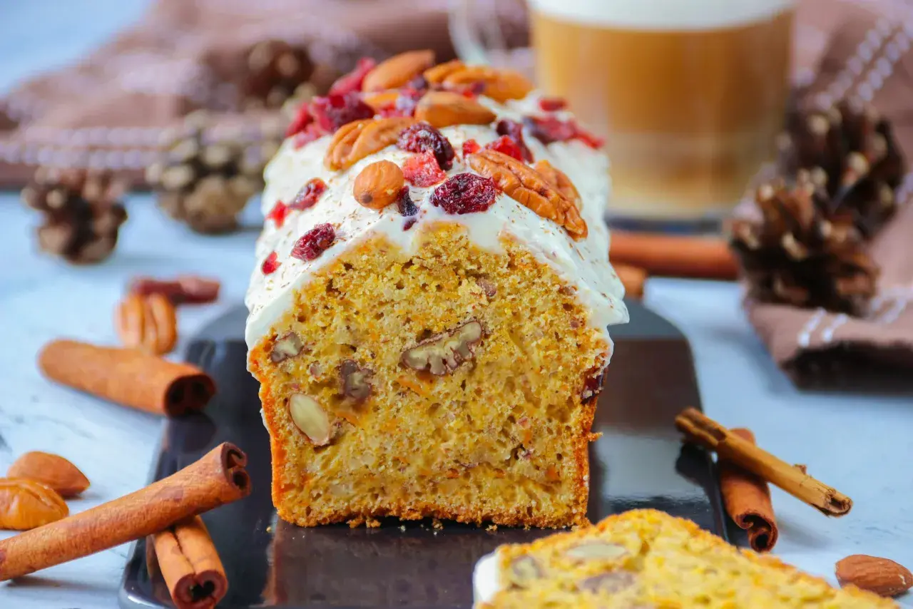 Un délicieux carotte cake glacé, garni de noix et de canneberges, prêt à être dégusté. Une recette parfaite pour le goûter.