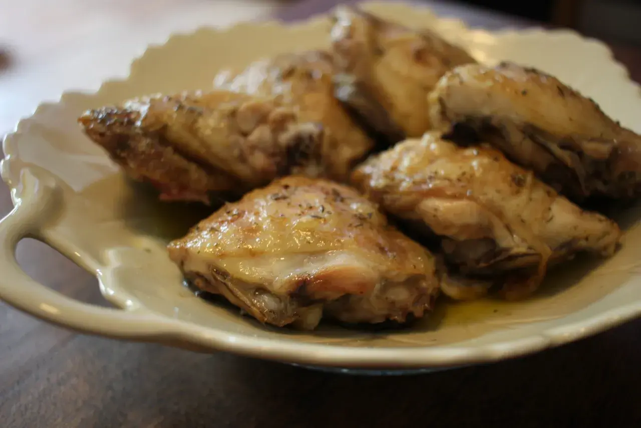 Plusieurs hauts de cuisse de poulet au four, dorés et assaisonnés d'herbes, reposent sur une assiette blanche festonnée.