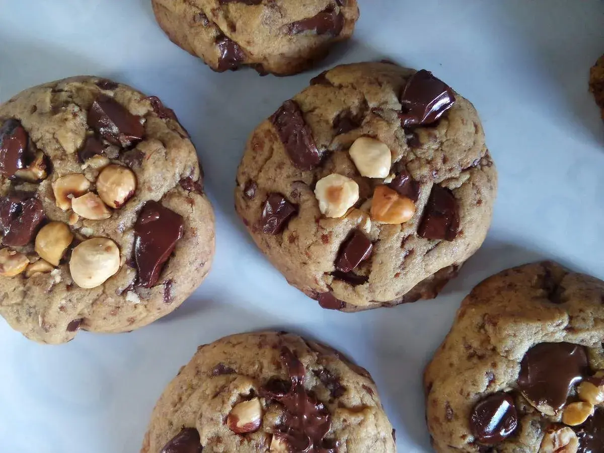 Gros plan sur des cookies américains faits maison, débordant de pépites de chocolat noir et de noisettes. Parfaits pour une recette de cookies américain gourmande.