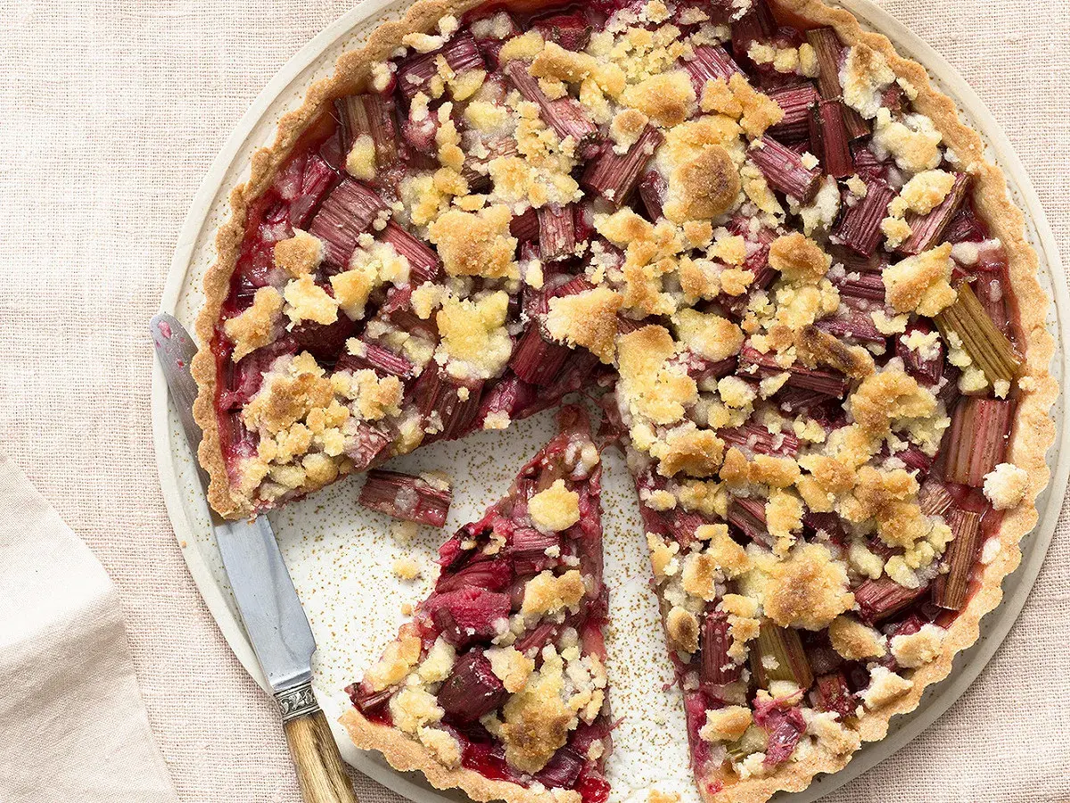 Tarte crumble à la rhubarbe, une délicieuse recette avec rhubarbe, garnie de morceaux de fruits rouges et d'une pâte croustillante.