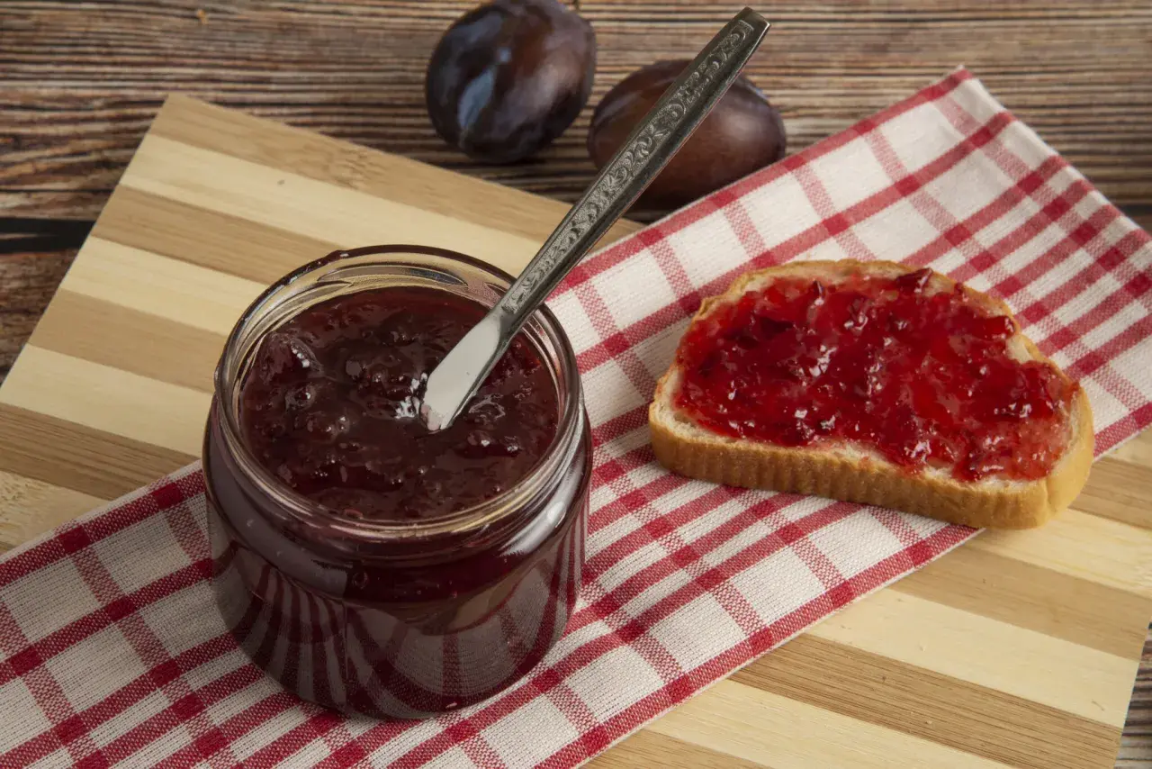 Un pot de confitures de quetsches maison, une tartine généreusement garnie et quelques quetsches sur une planche en bois.