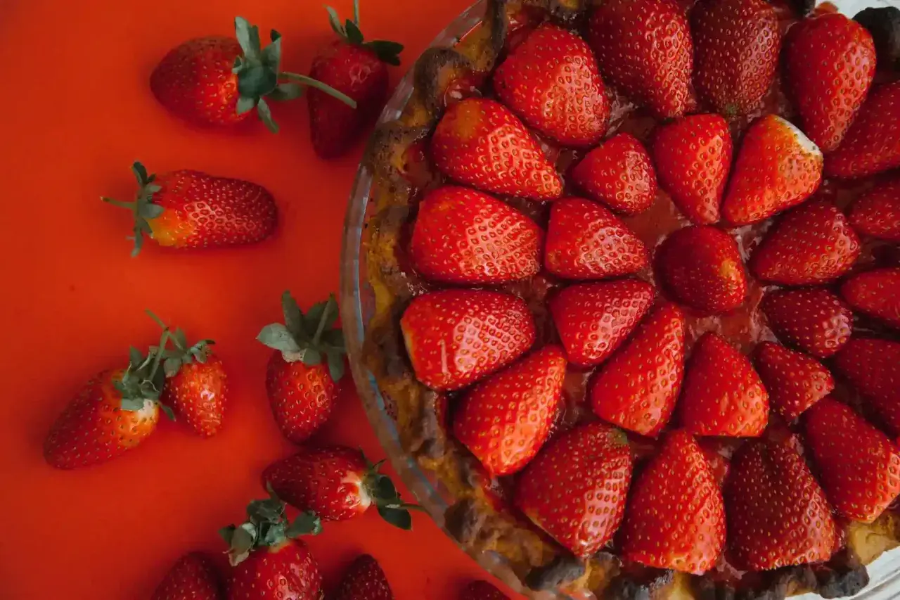 Tarte aux fraises sans crème pâtissière, garnie de fruits rouges frais sur fond rouge. Un délice simple et fruité.