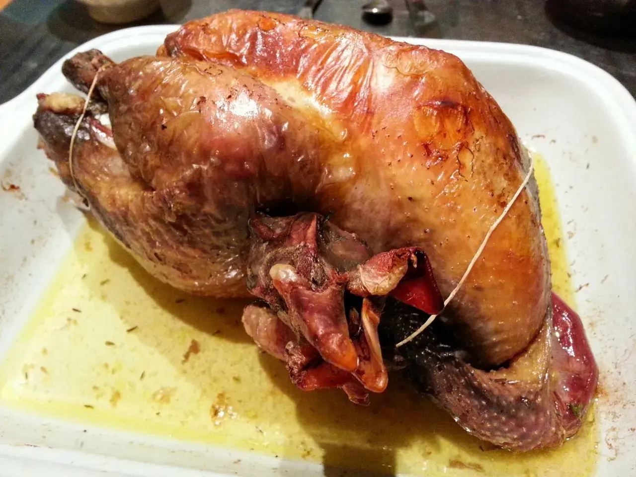 Une pintade au four, dorée et juteuse, repose dans un plat blanc, baignant dans son jus savoureux.