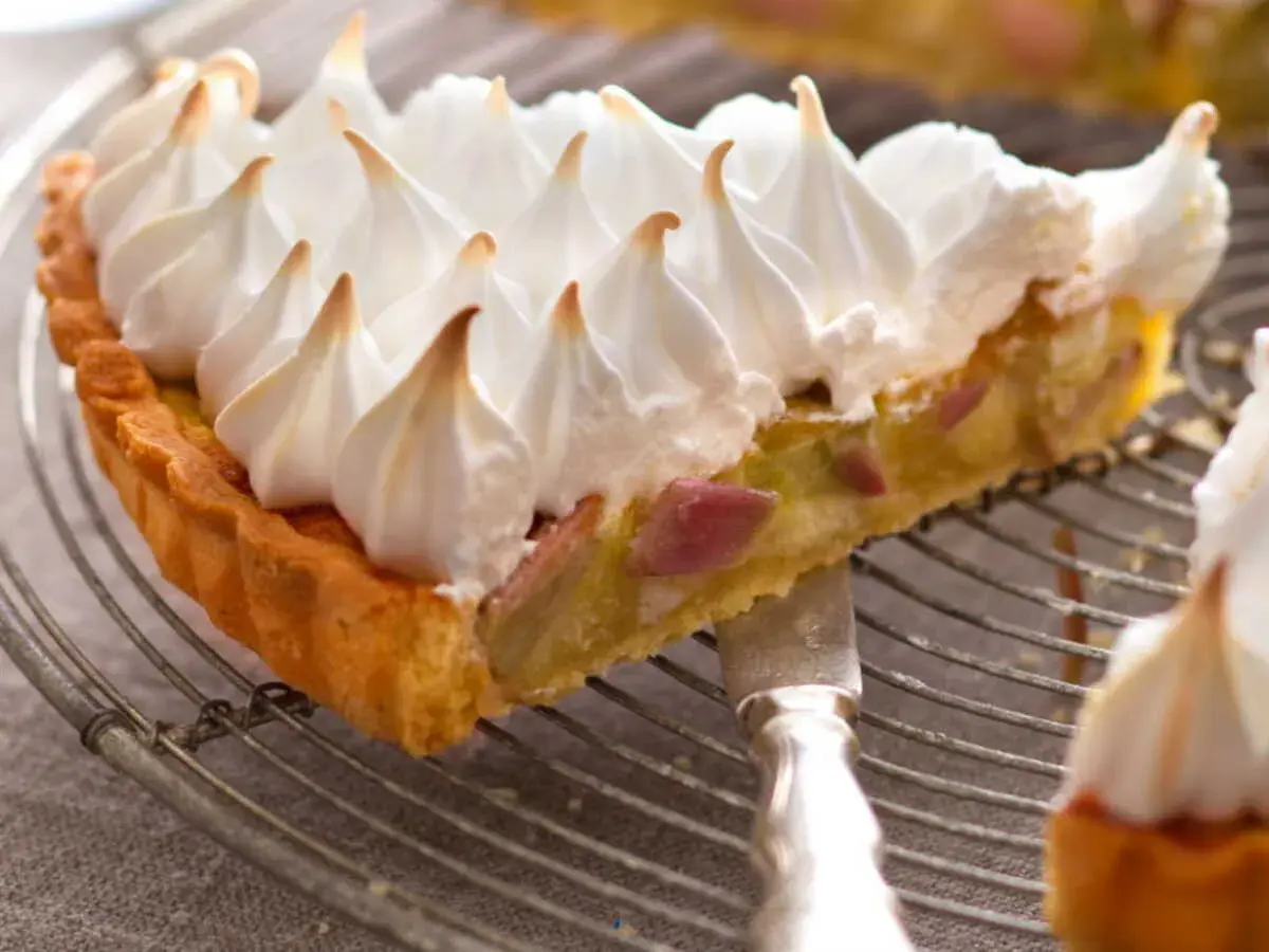 Une part de tarte rhubarbe meringuée, avec sa croûte dorée et sa garniture acidulée, surmontée d'une meringue légère et aérienne.