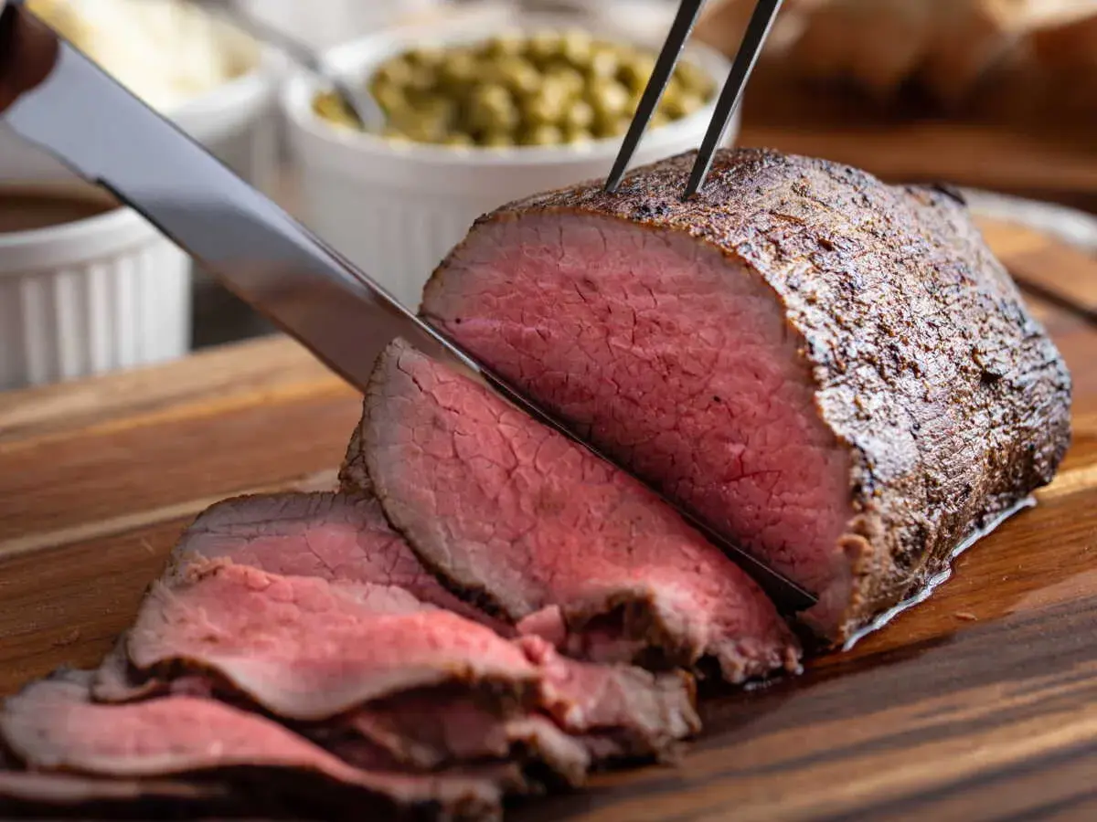 Un délicieux rôti de boeuf, coupé en fines tranches rosées, est prêt à être servi avec des accompagnements.