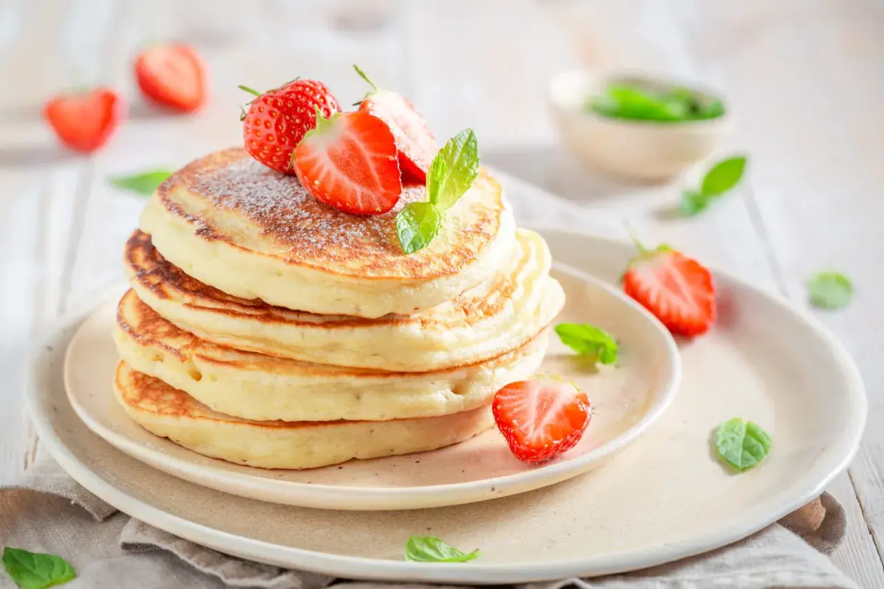 Pile de pancakes moelleux, parsemés de sucre glace et ornés de fraises fraîches et de menthe. Un délice digne des pancakes Cyril Lignac.
