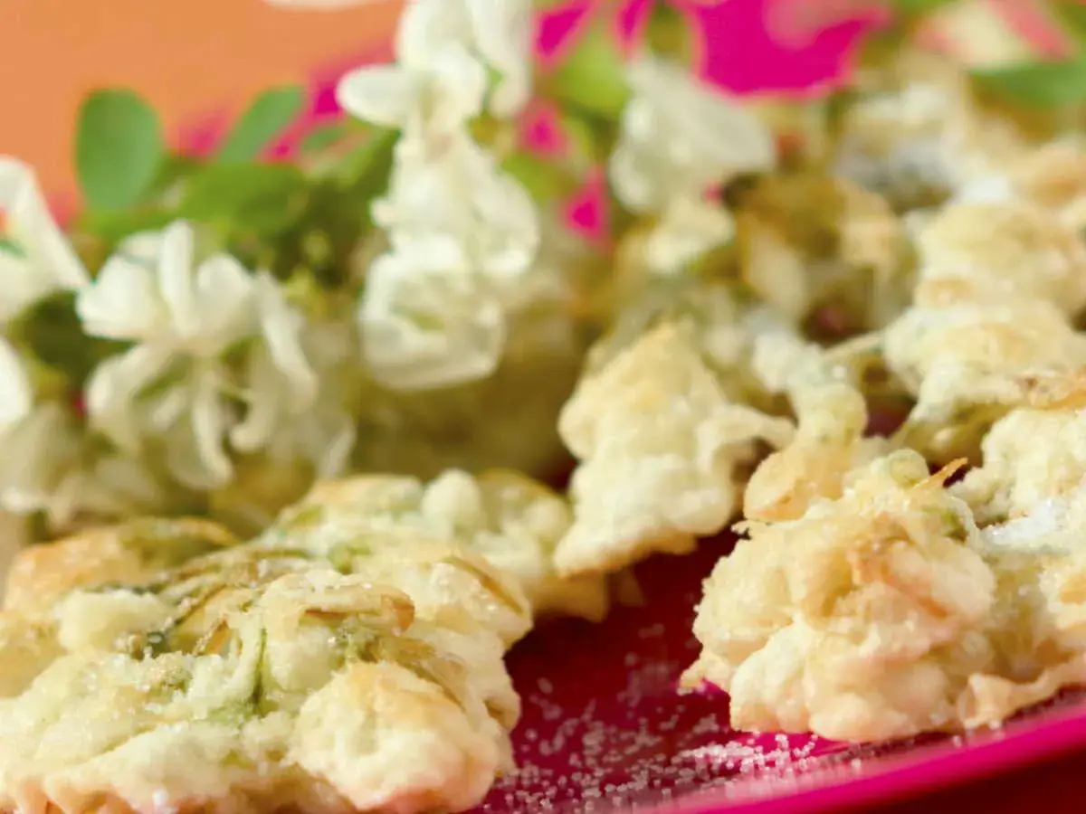 Délicieux beignets de fleur d'acacia à la poêle, saupoudrés de sucre, avec des fleurs fraîches en arrière-plan.