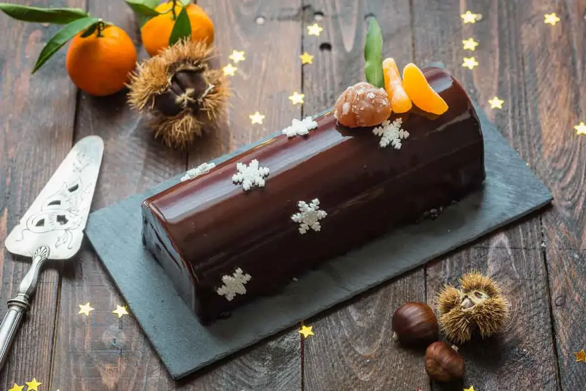 Bûche marron glacé, décorée de flocons et de quartiers de clémentine, évoquant la magie de Noël.