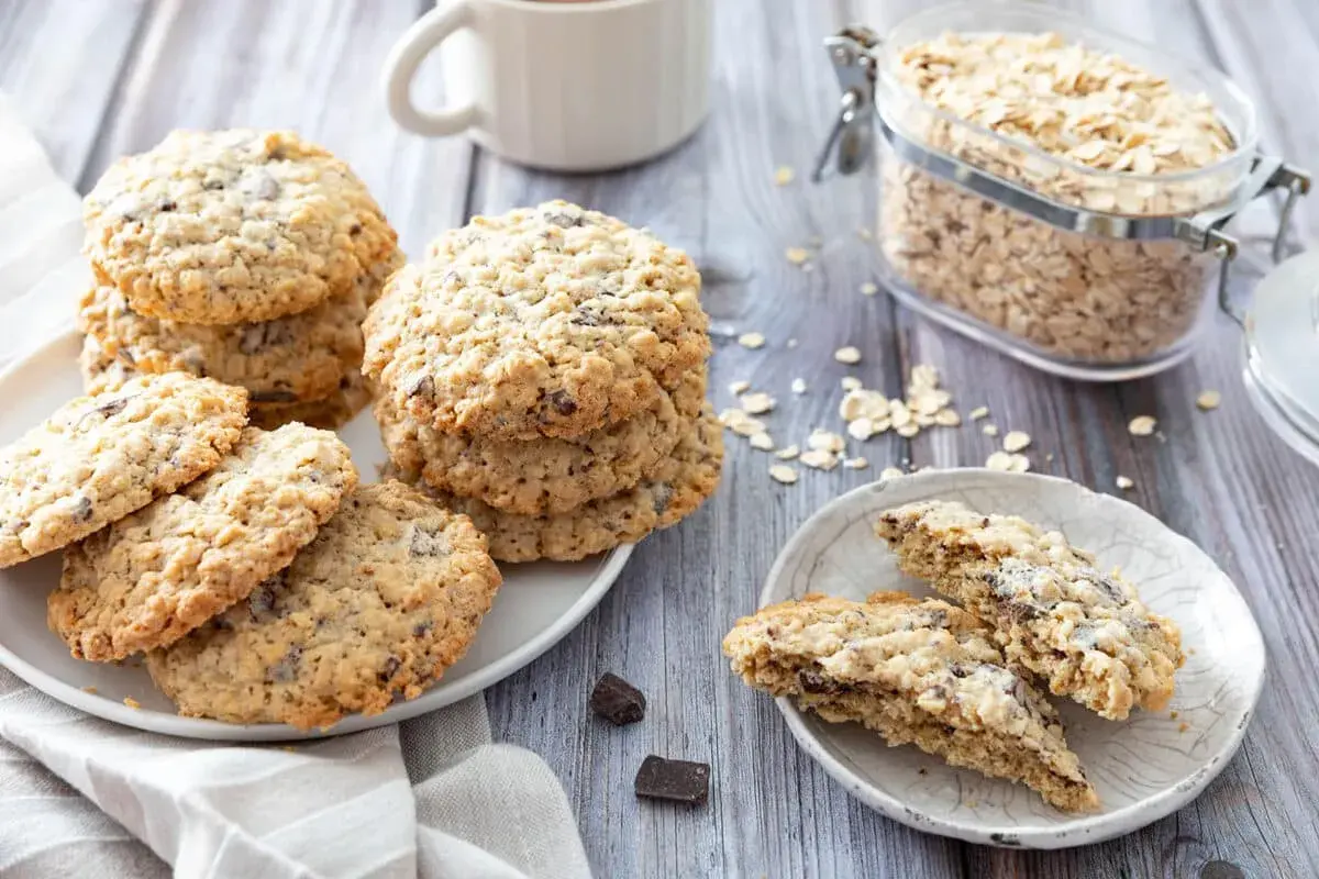 Des biscuits flocons d'avoine aux pépites de chocolat, empilés sur une assiette, avec un bocal de flocons d'avoine en arrière-plan.