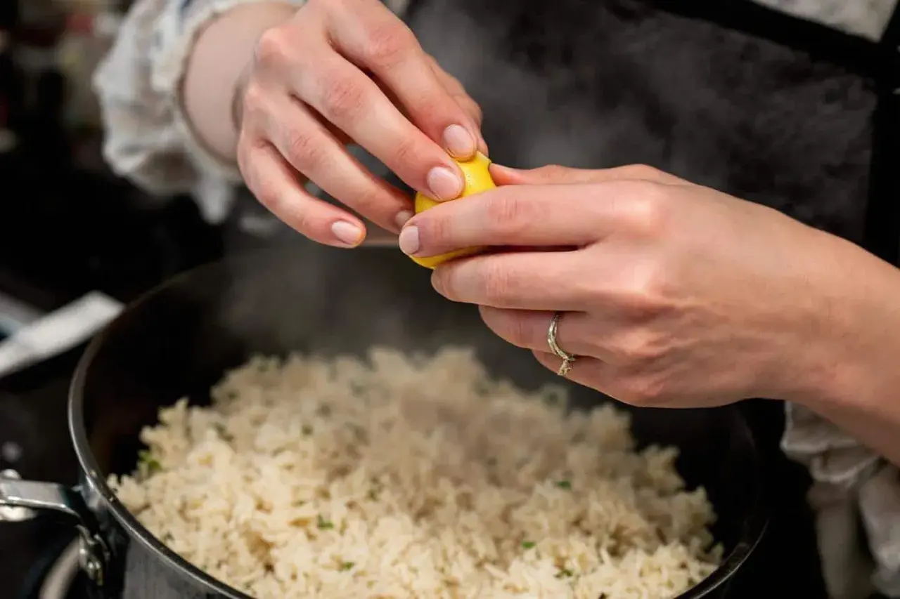 Cuisson du riz rouge : une main presse un quartier de citron sur le riz fumant dans une casserole.
