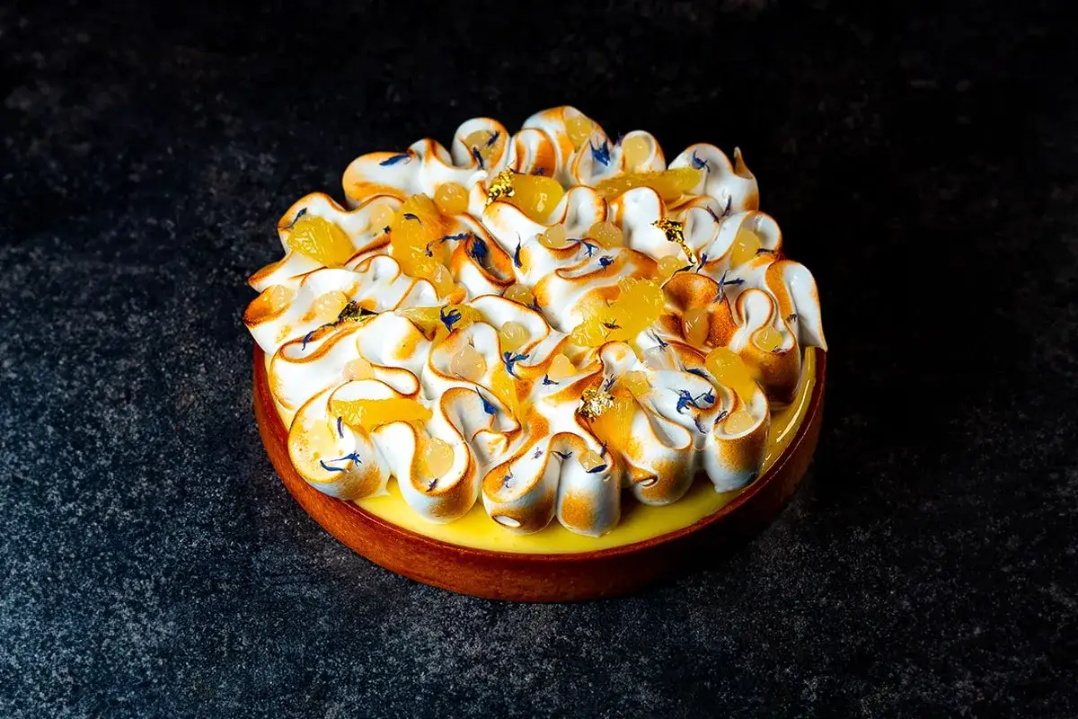 Tarte citron meringuée aux zestes et perles d'agrumes, décorée de feuilles d'or. Une invitation à la gourmandise.