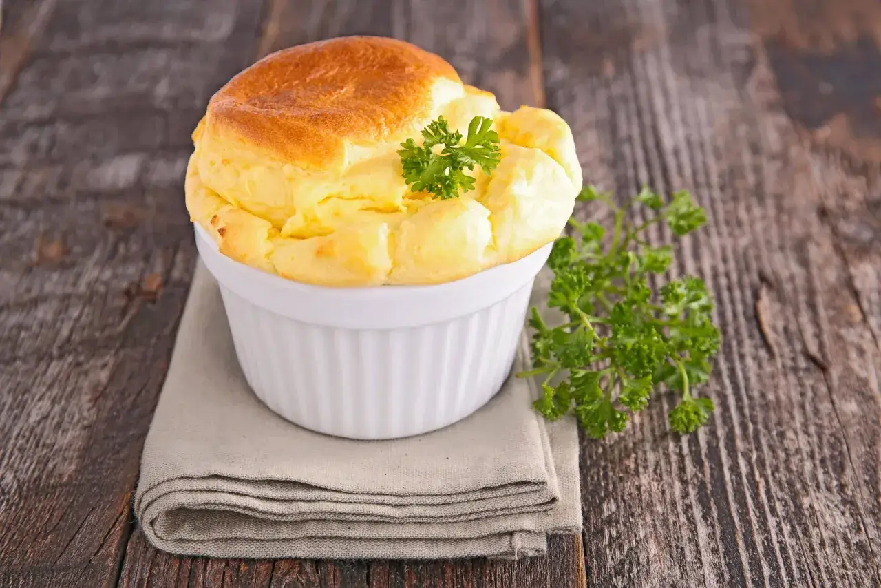 Soufflé au fromage doré et aérien dans un ramequin blanc, garni de persil frais. Une invitation à découvrir la recette du soufflé au fromage.