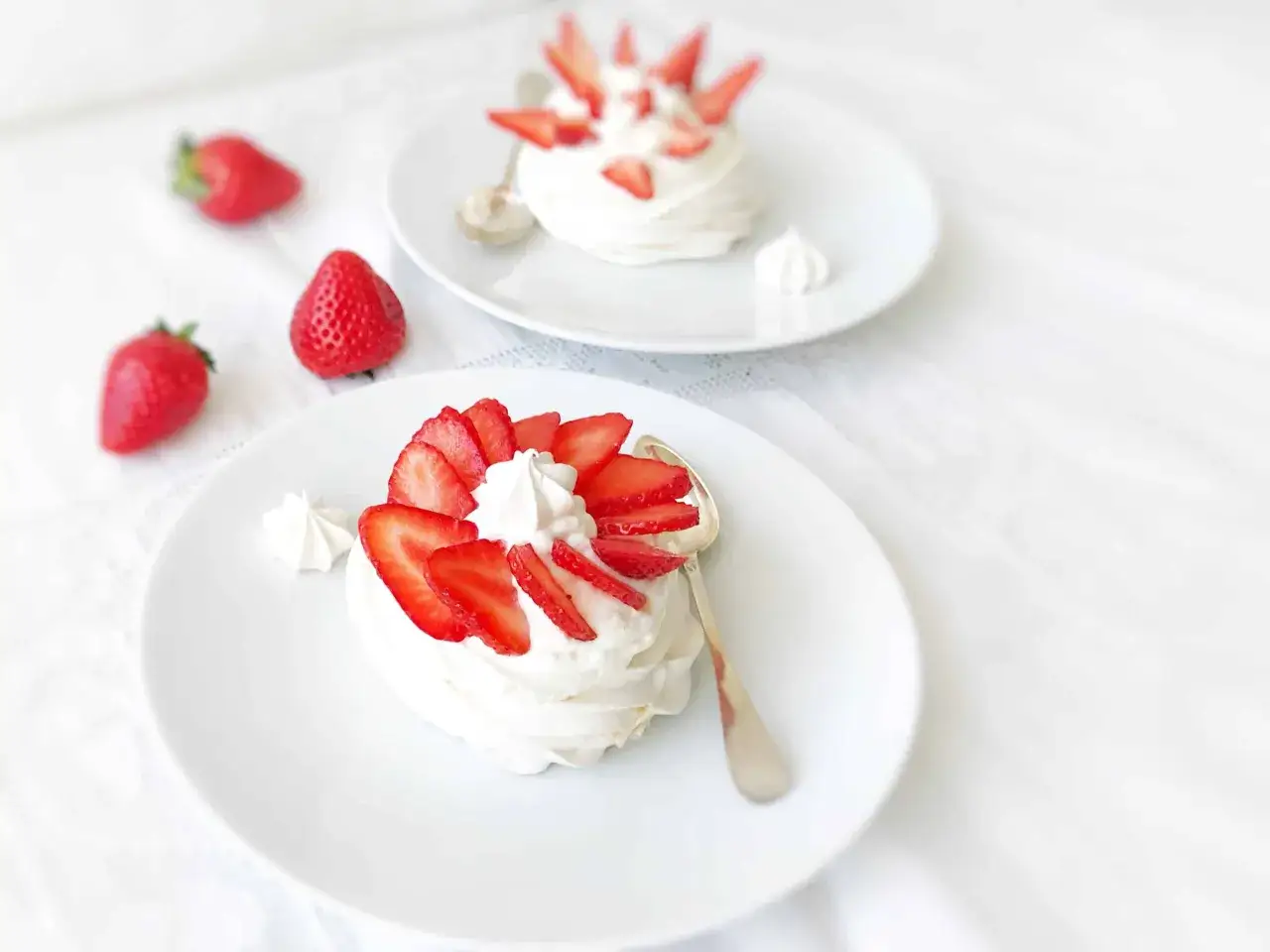 Deux pavlovas individuels garnis de crème fouettée et de fraises fraîches, prêts à être dégustés. Une recette pavlova simple et délicieuse.