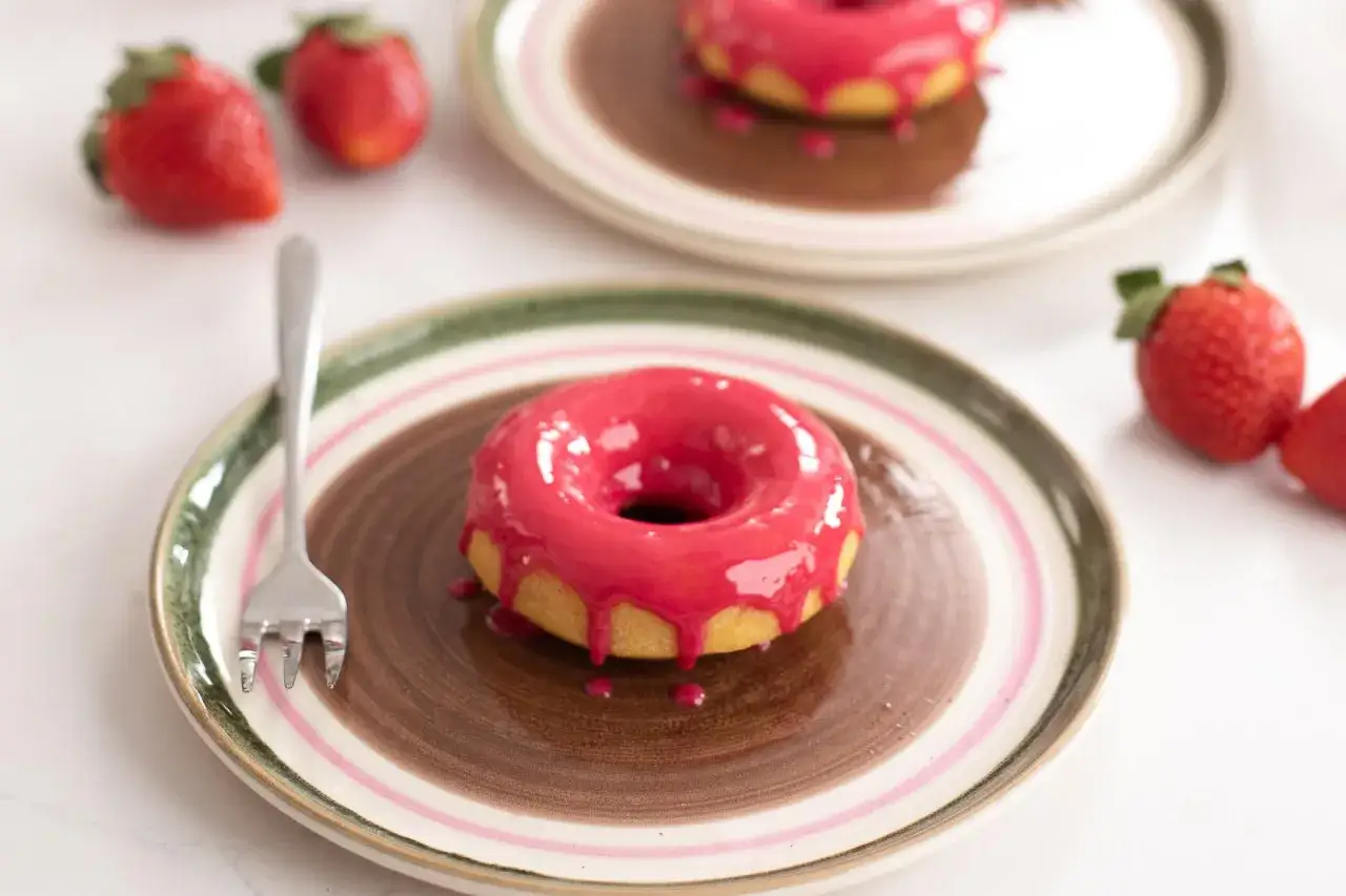 Donuts roses brillants sur assiette, accompagnés de fraises. Une invitation à découvrir une recette donuts professionnel.