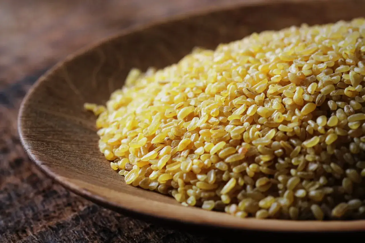 Grains de boulgour dor&eacute;s dans un bol en bois, pr&ecirc;ts pour la cuisson.