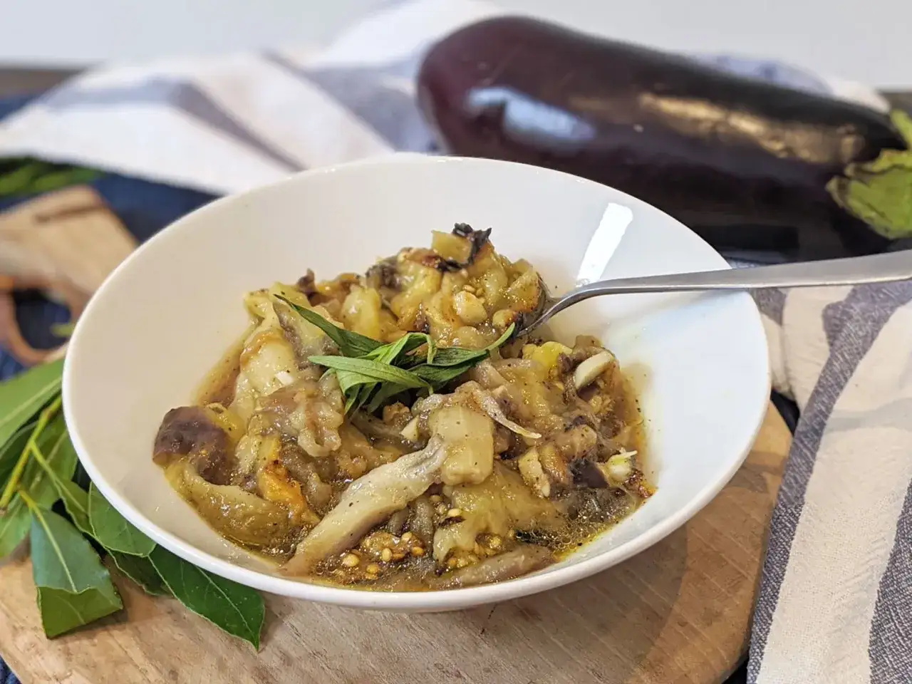 Un bol de caviar d'aubergine, garni d'herbes fraîches, avec une aubergine entière en arrière-plan.