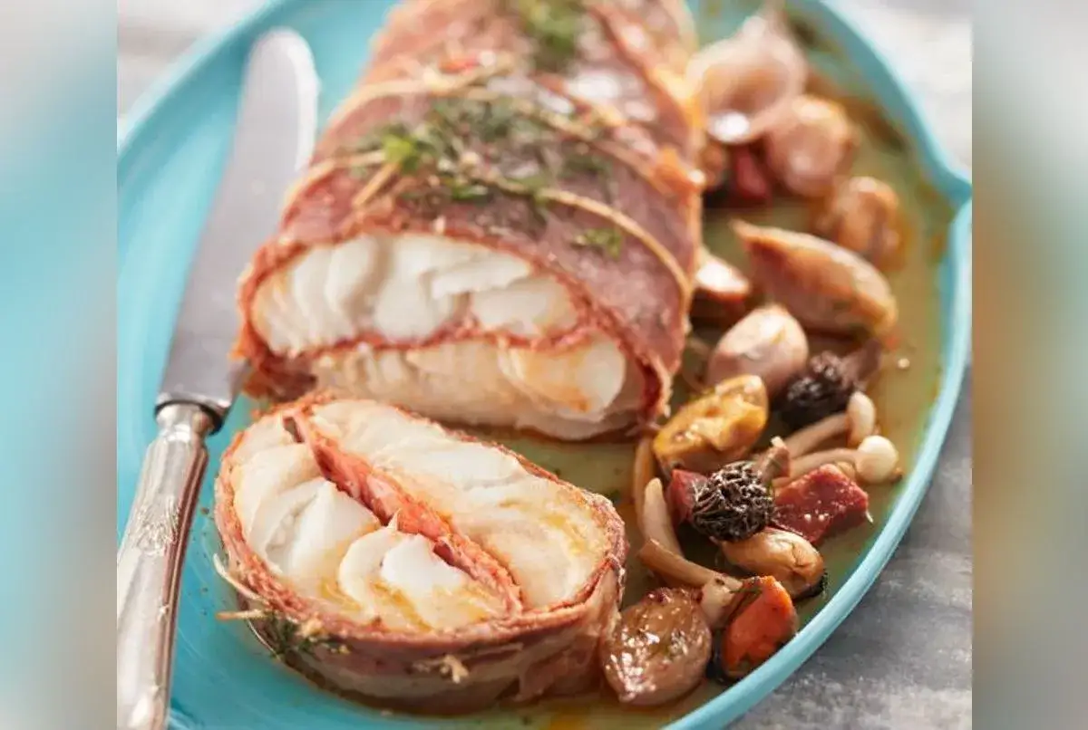 Dos de cabillaud au four, enveloppé de lard, servi avec des champignons et des moules. Un plat savoureux et élégant.