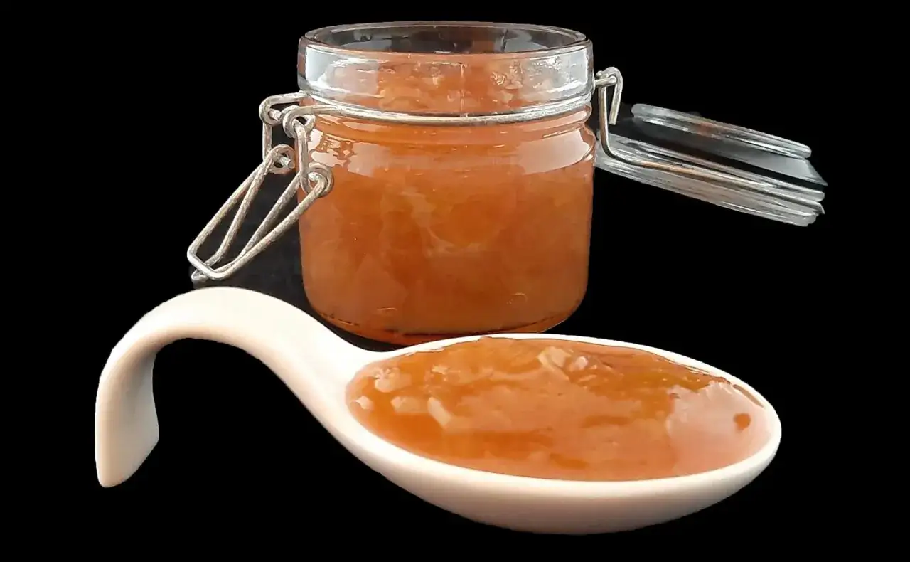 Un pot de confiture de rhubarbe maison, avec une cuillère en porcelaine remplie de cette délicieuse confiture.