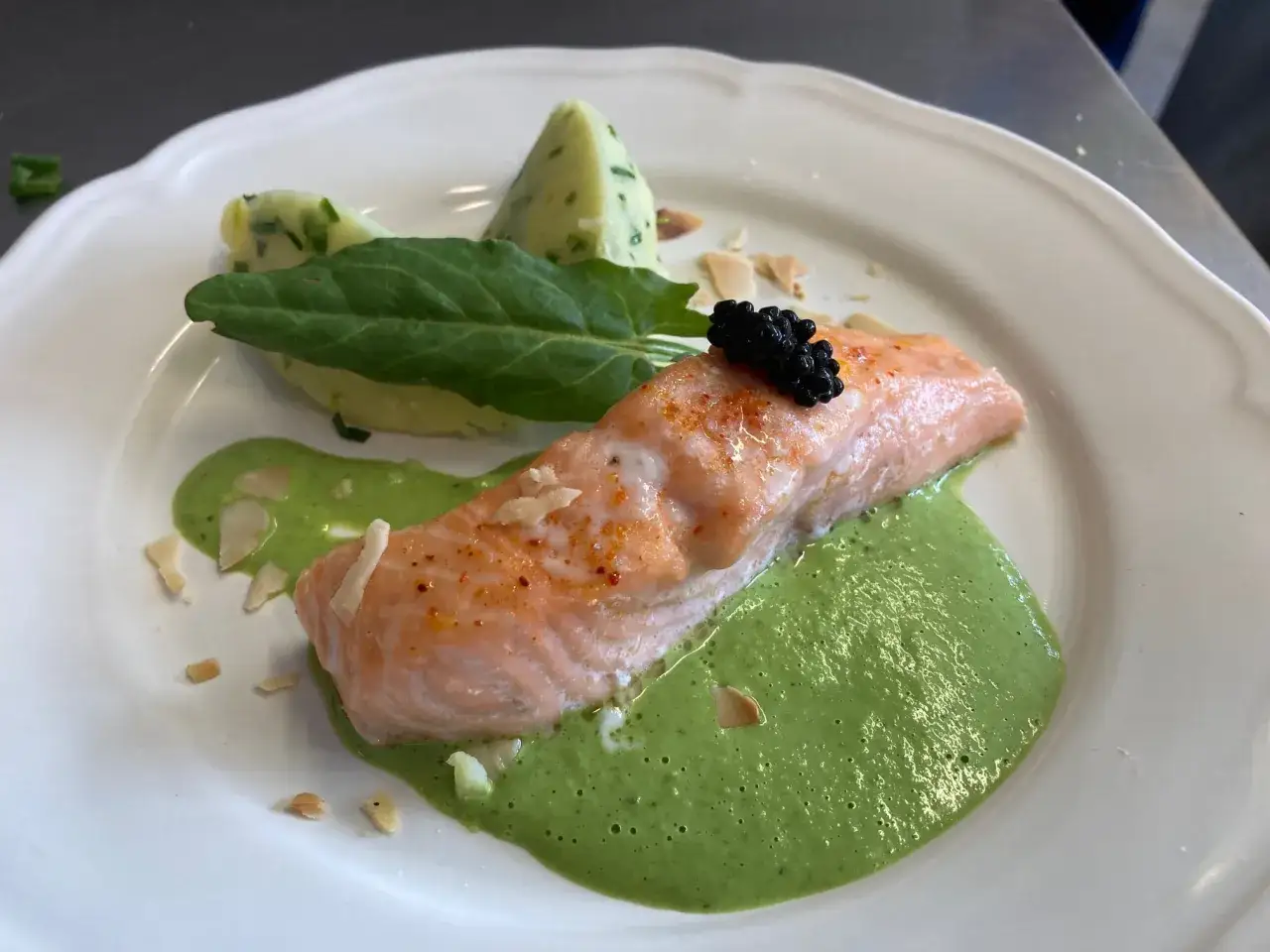 Filet de saumon poêlé, garni de caviar, sur une sauce à l'oseille crémeuse, accompagné de purée de pommes de terre et d'une feuille d'épinard.
