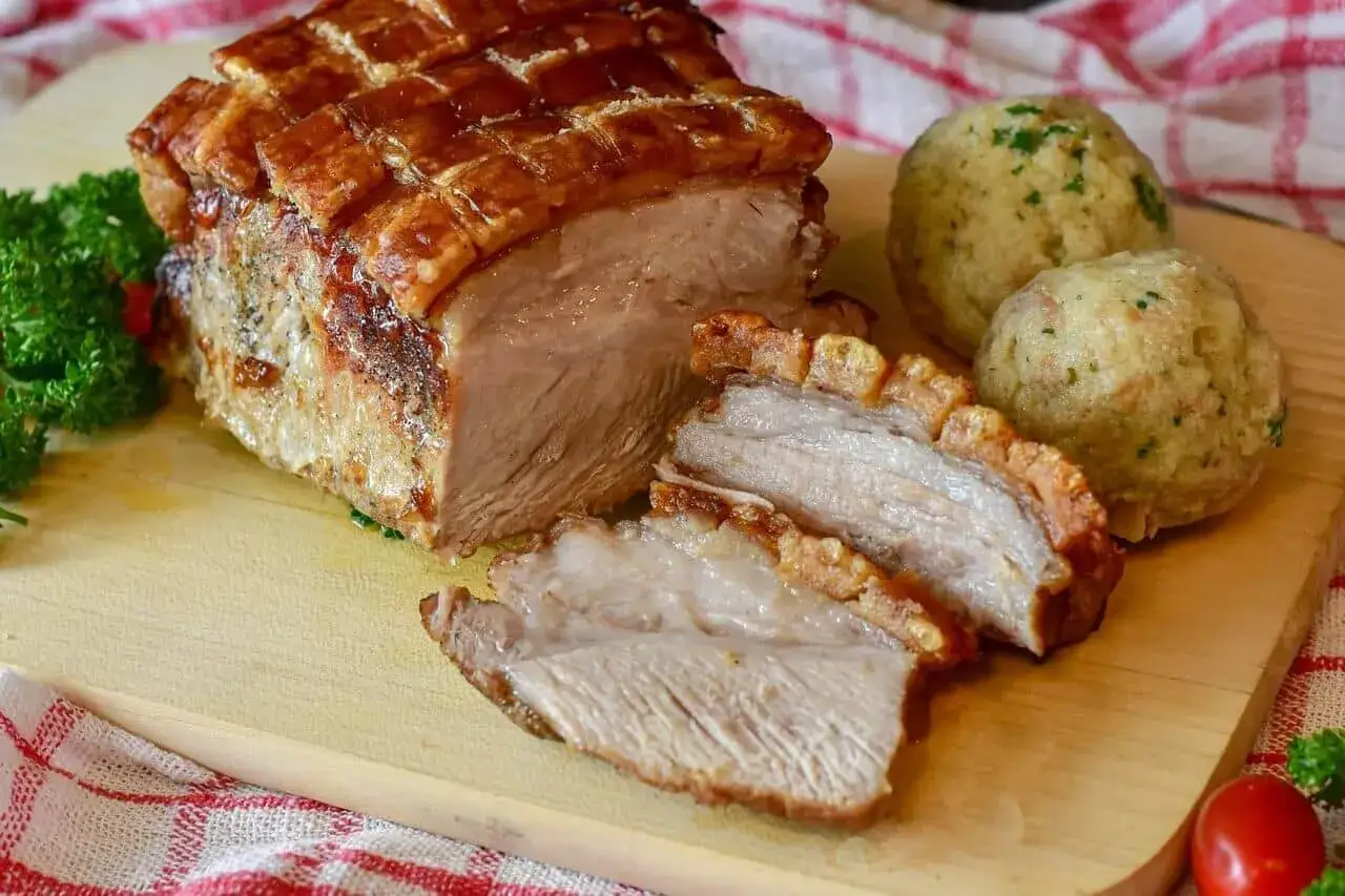 Un délicieux roti de porc au four, croustillant et juteux, servi avec des boules de pain et du persil.