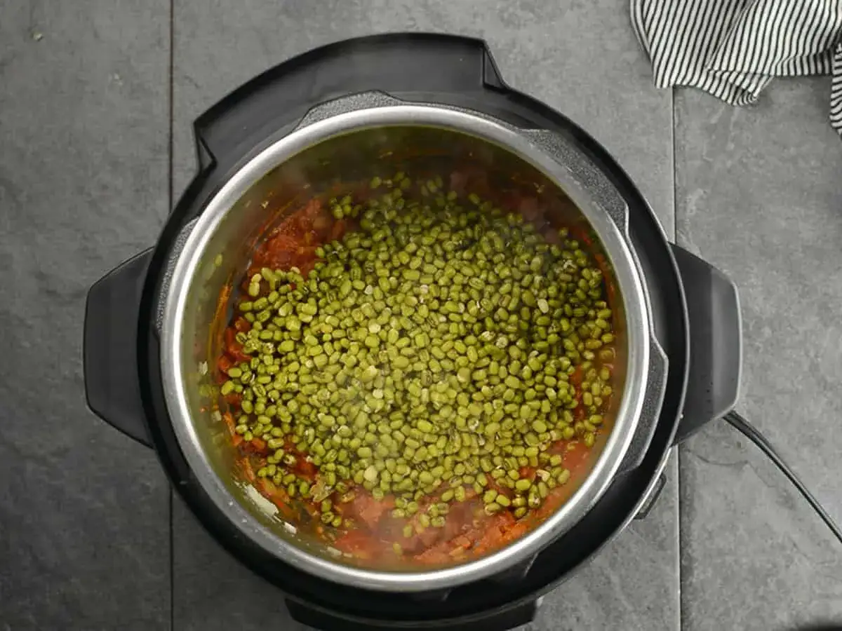 Cuisson de haricots mungo dans une cocotte minute, avec une sauce tomate en dessous.