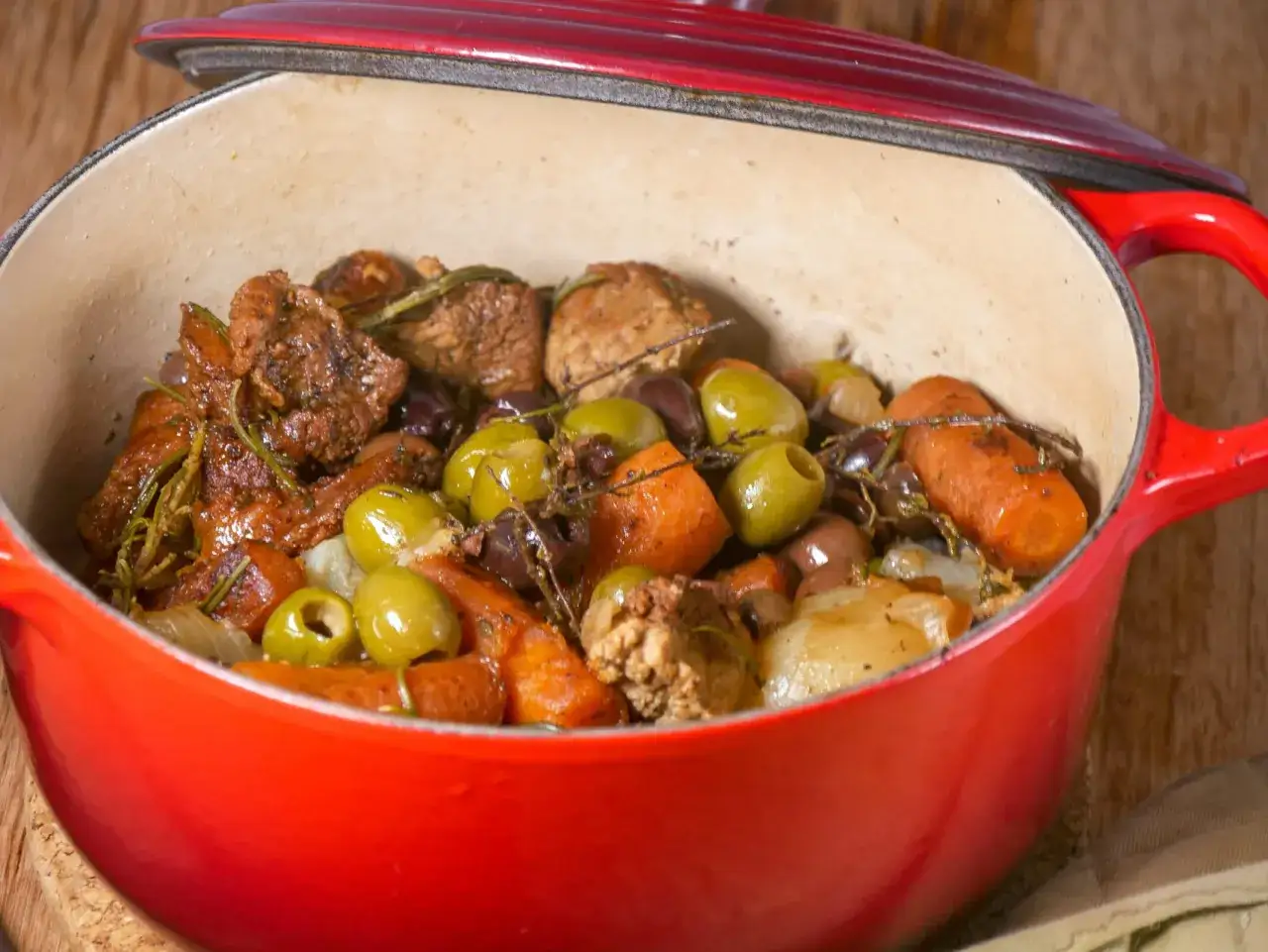 Un d&eacute;licieux saut&eacute; de veau mijote dans une cocotte rouge, avec des olives, des carottes et des herbes aromatiques.