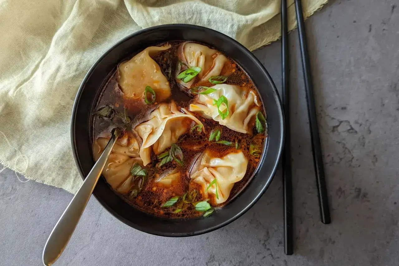 Un bol de soupe raviolis chinois, garni de ciboule fra&icirc;che, pr&ecirc;t &agrave; &ecirc;tre d&eacute;gust&eacute; avec des baguettes.