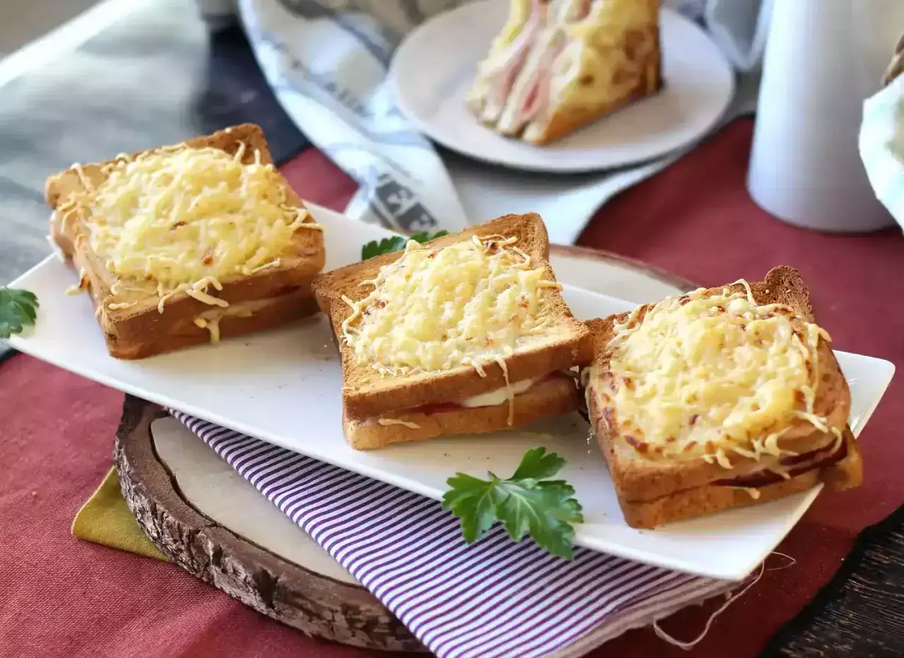 Trois croque monsieur dorés et gratinés, préparés à l'airfryer, sur une assiette blanche avec du persil.