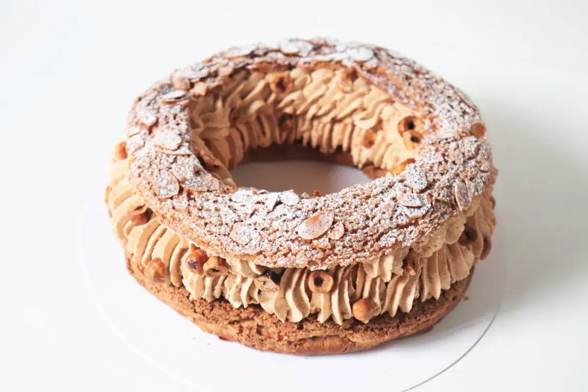 Un Paris-Brest rond, garni de crème pralinée et parsemé d'amandes effilées et de noisettes.