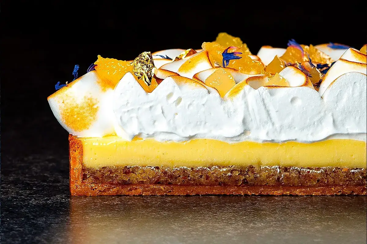 Une tranche de tarte au citron exceptionnelle, avec une meringue dorée, des zestes d'orange et une touche d'or comestible.