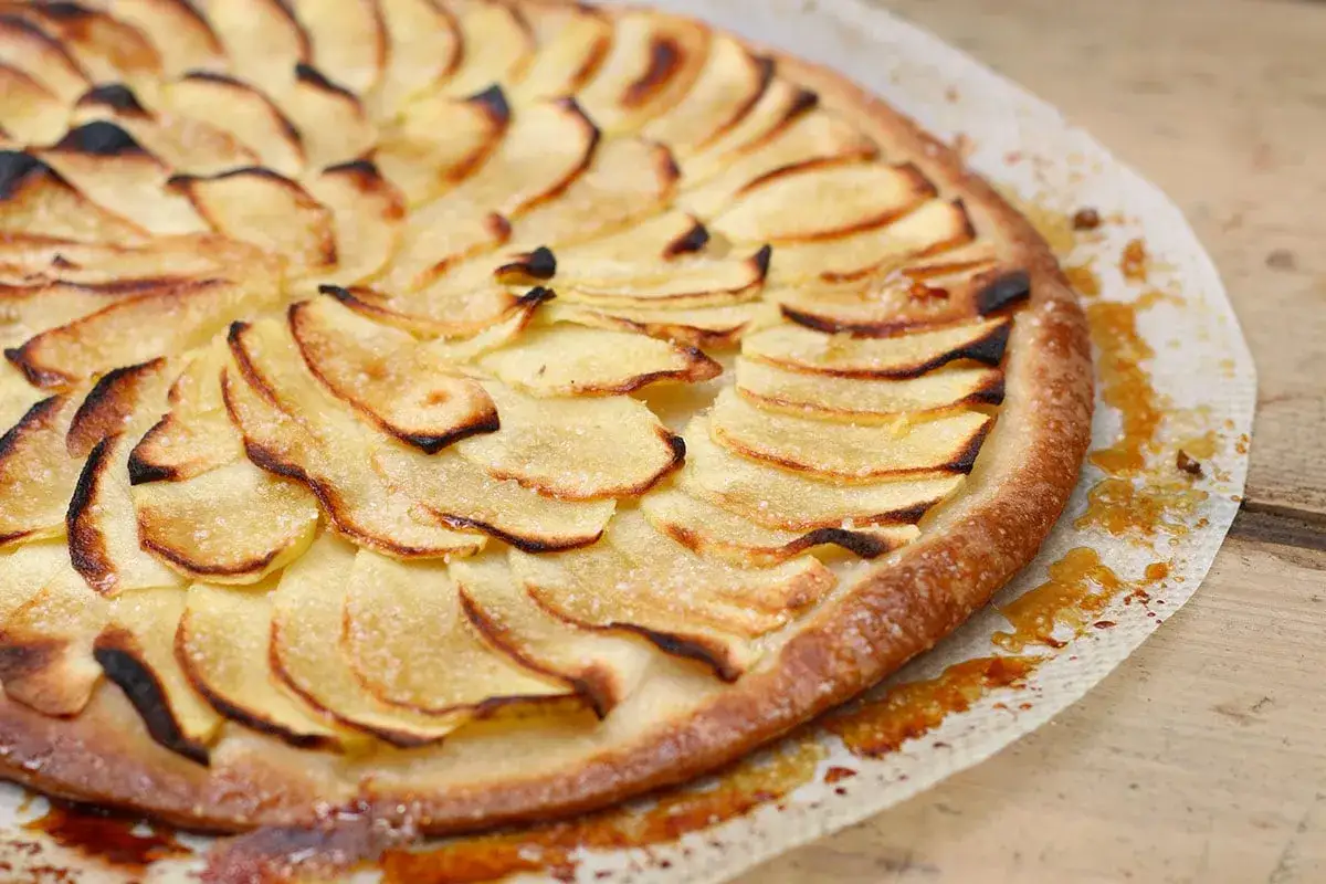Une tarte aux pommes simple, joliment décorée de fines tranches de pommes dorées et légèrement caramélisées, posée sur une planche en bois.