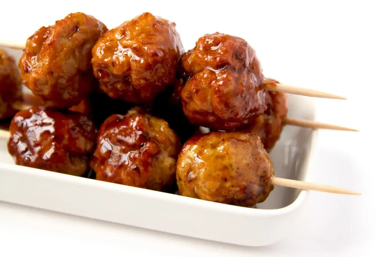 Boulettes de poulet yakitori, nappées d'une sauce caramélisée, servies sur des brochettes en bois dans un plat blanc.