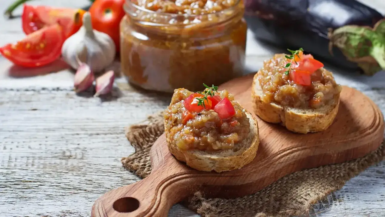 Deux toasts garnis de le vrai caviar d'aubergine, garni de tomates fraîches et d'une touche de thym, sur une planche en bois.