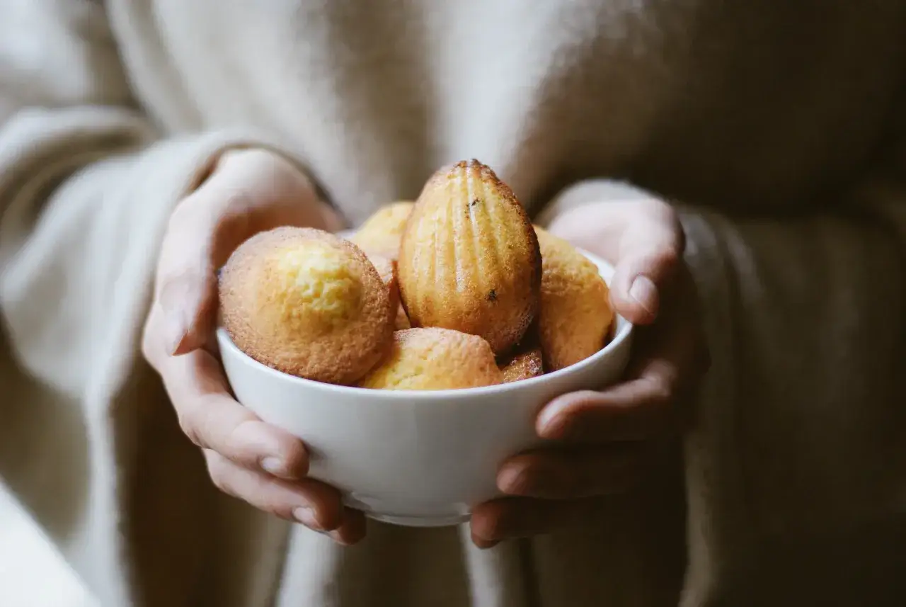 Mains tenant un bol de madeleines dorées, parfaites pour une recette facile.