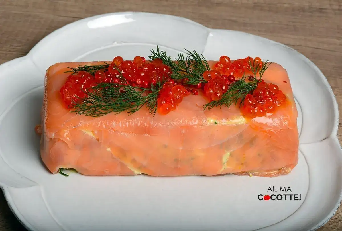 Une terrine de saumon, chef étoilé, ornée de baies rouges et d'aneth, sur une assiette blanche.