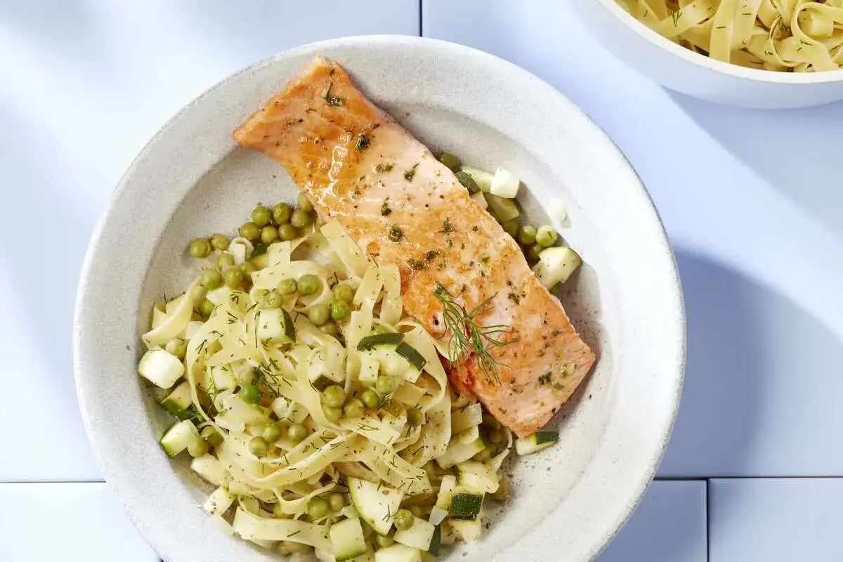 Un plat de tagliatelles au saumon, garni de petits pois et de courgettes, avec une touche d'aneth frais.