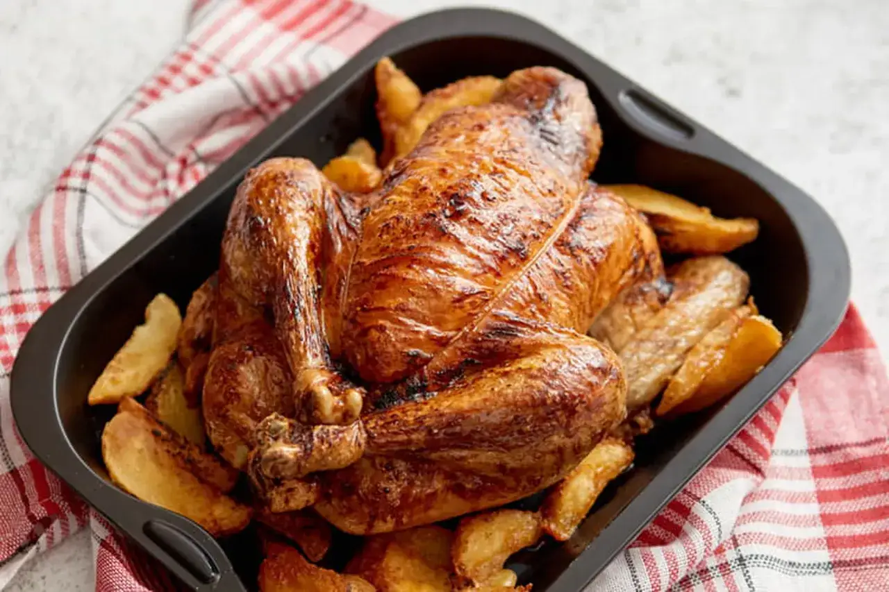Un appétissant coquelet au four, doré et croustillant, servi avec des quartiers de pommes de terre rôtis dans un plat noir.