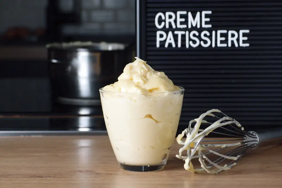 Un verre rempli de crème pâtissière onctueuse, avec un fouet couvert de cette délicieuse préparation. Le mot 