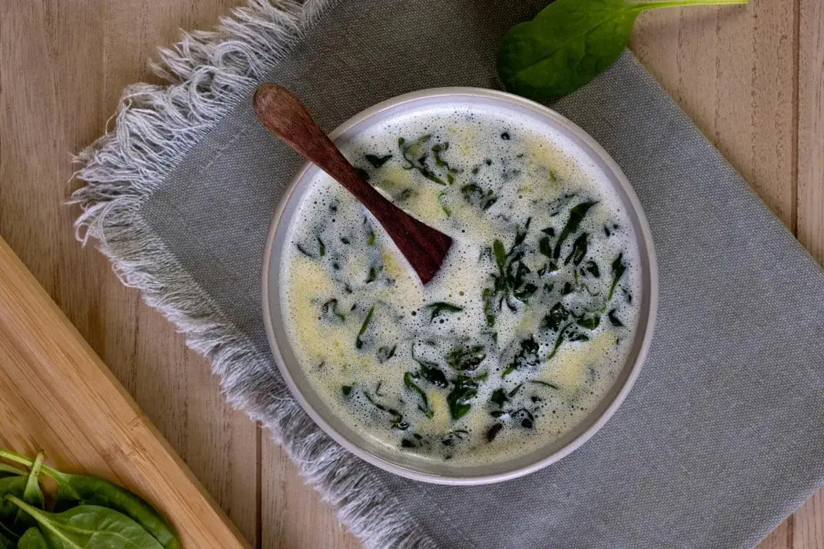 Sauce oseille grand chef, crémeuse et onctueuse, garnie de feuilles d'épinards frais. Une cuillère en bois repose dans le plat.