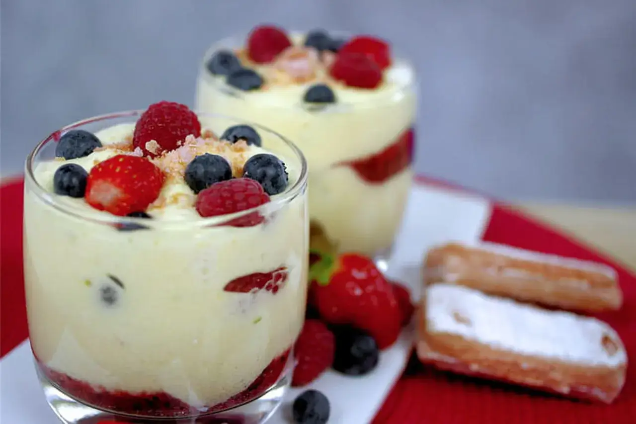 Deux verrines de tiramisu fraise, garnies de fruits rouges frais et de biscuits saupoudrés de sucre glace.
