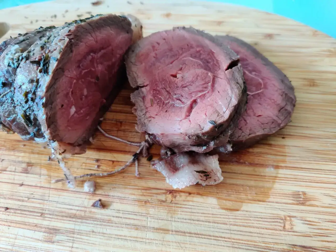 Tranches de rôti de bœuf juteux, cuit au four, assaisonné d'herbes, sur une planche à découper en bois.