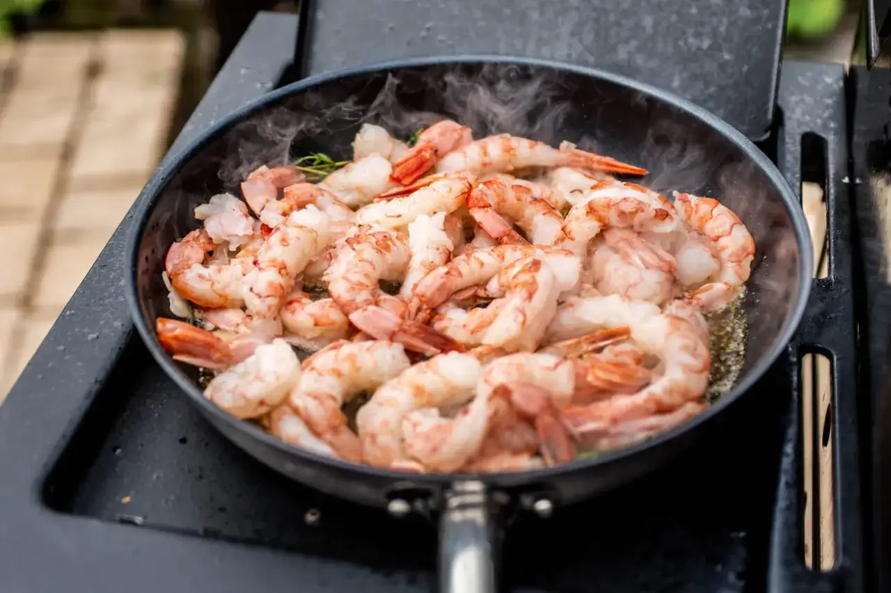 Cuisson de crevettes grises dans une poêle, dégageant une vapeur savoureuse. Un délice à portée de main.