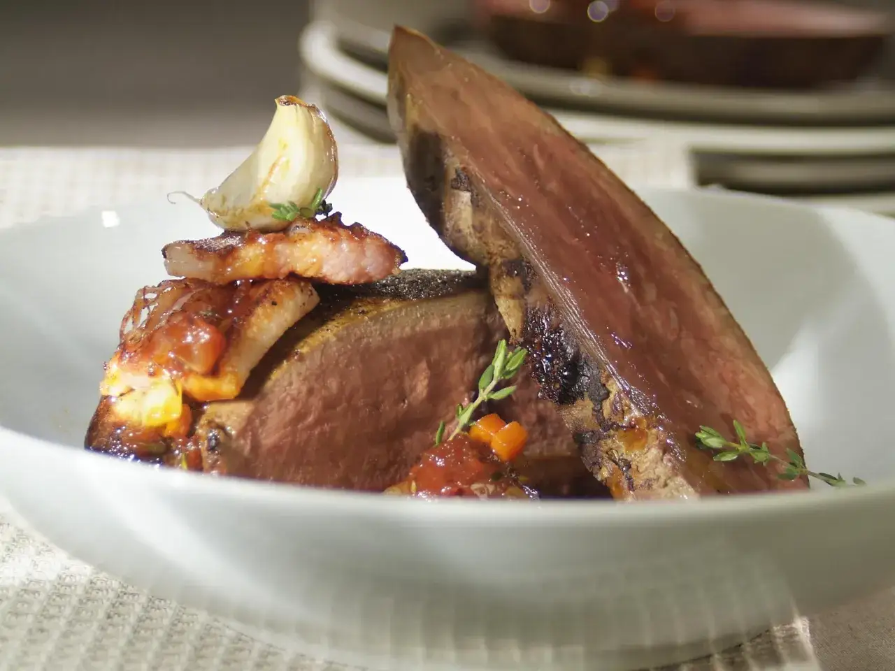 Tranches de viande savoureuses, garnies d'une sauce aux tomates et d'une t&ecirc;te d'ail r&ocirc;tie, un accompagnement foie de veau parfait.