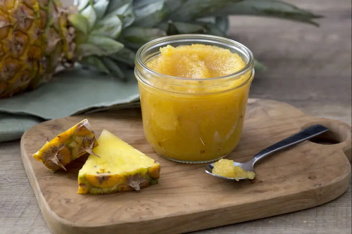 Un pot de confiture d'ananas maison, avec des morceaux d'ananas frais et une cuillère remplie de cette délicieuse confiture.